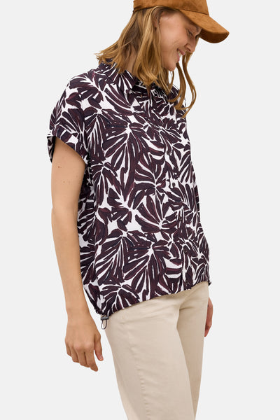 Bordeaux blouse met korte mouwen van CECIL, met blad-bloemenpatroon, gedragen met een beige broek en een bruine pet.