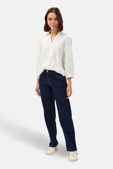 Chemisier blanc à manches courtes de CECIL, porté avec un pantalon bleu foncé et des baskets blanches.