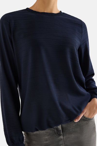 Blouse à manches longues bleue by CECIL, avec une texture subtile et portée avec un jean gris.
