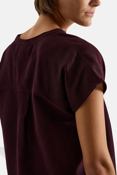 Bordeaux short-sleeve blouse with relaxed fit and rounded neckline, side view showing textured fabric and soft drape