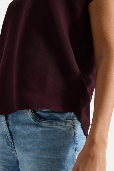 Bordeaux short-sleeve blouse with relaxed fit and soft fabric, worn with light blue jeans, side view close-up