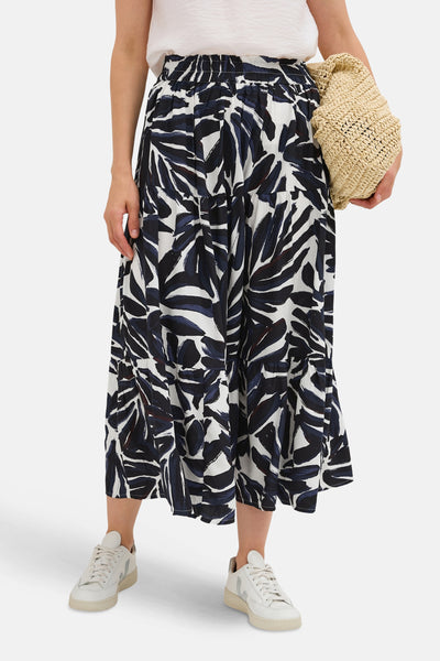 Jupe longue multicolore de CECIL, à motif floral abstrait, avec détails froncés et chaussures de sport blanches.
