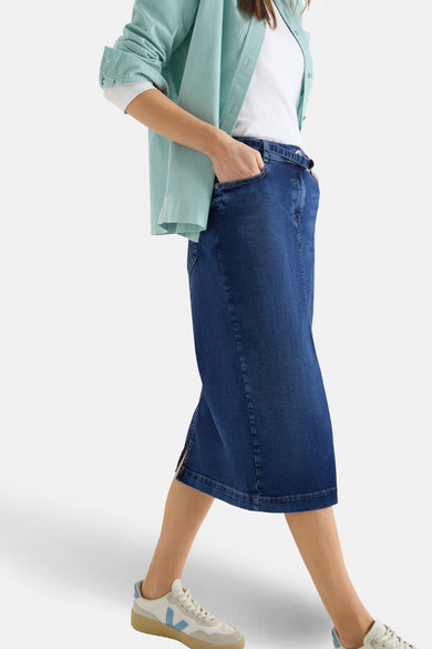 Jupe midi en denim bleu, de CECIL, avec une fente latérale et portée avec une chemise turquoise.
