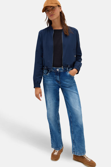 Wijde spijkerbroek in middieblauw denim van CECIL, gedragen met een marineblauwe jas en bruine sneakers.