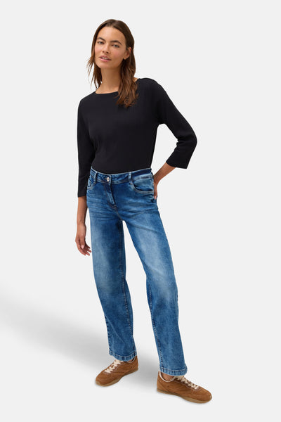 Jean large en denim bleu moyen de CECIL, porté avec un haut noir à manches trois-quarts et des baskets marron.
