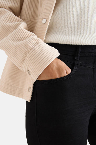 Jean slim en denim noir de CECIL, avec une main dans la poche, porté avec un pull.
