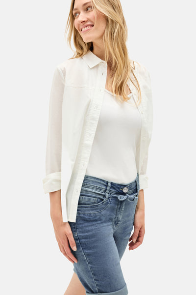 Bermuda en denim bleu clair de CECIL, porté avec un t-shirt blanc et une chemise blanche.