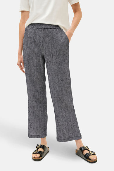 Pantalon bleu à motif texturé by CECIL, avec poches et porté avec un t-shirt blanc et des sandales noires.
