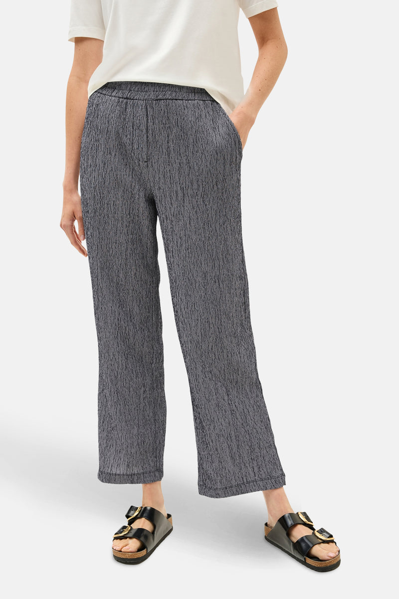 Pantalon bleu à motif texturé by CECIL, avec poches et porté avec un t-shirt blanc et des sandales noires.
