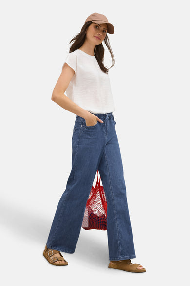 Jean large en denim bleu moyen de CECIL, porté avec un haut blanc et des sandales marron.