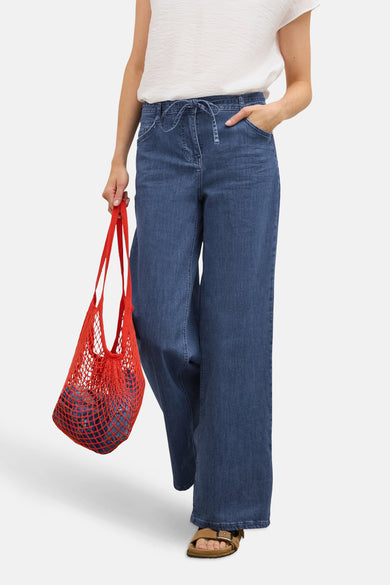 Jean large en denim bleu moyen de CECIL, avec cordon à la taille et porté avec un sac en filet rouge.
