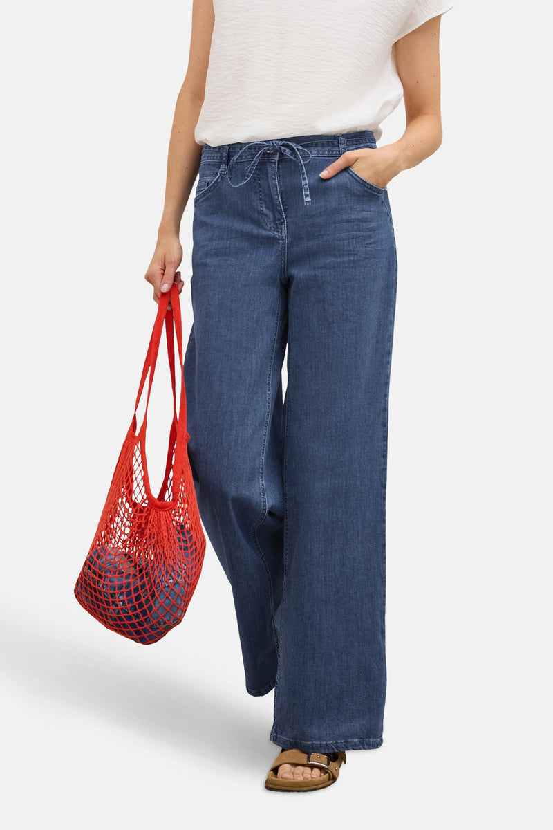 Jean large en denim bleu moyen de CECIL, avec cordon à la taille et porté avec un sac en filet rouge.
