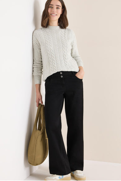 Jean large en denim noir par CECIL, avec des boutons à la taille, porté avec un pull en maille torsadée et un sac fourre-tout.
