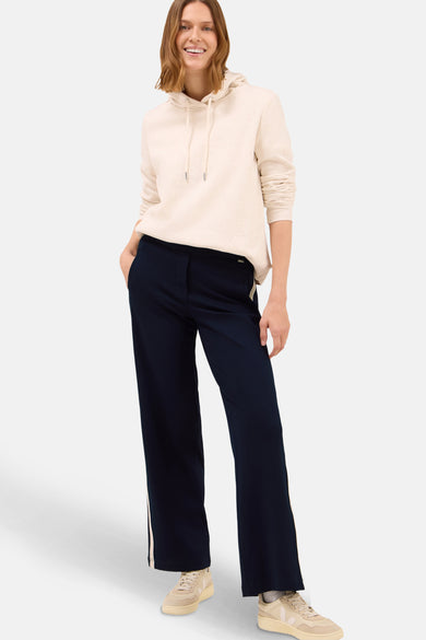 Effengekleurde blauwe broek van CECIL, met een crèmekleurige bies aan de zijkant, gedragen met een beige trui en sneakers.