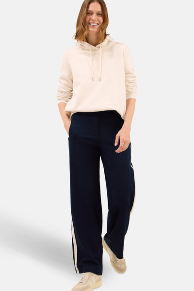 Blauwe broek van CECIL, wijd met een beige zijstreep en gedragen met een beige hoodie en sneakers.