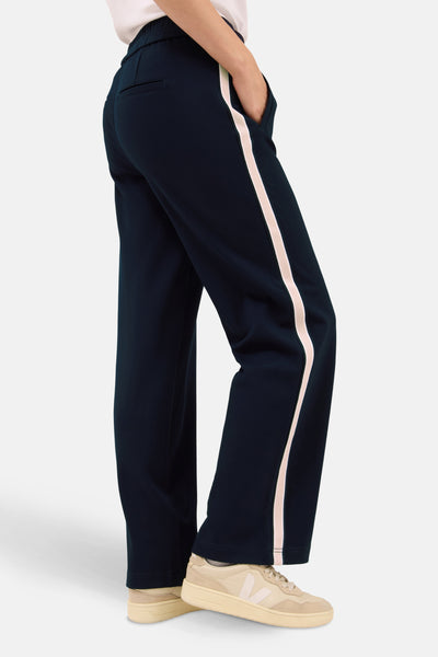 Pantalon bleu avec bande rose par CECIL, coupe ample, porté avec des baskets beiges.