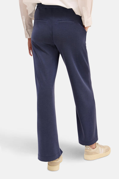 Pantalon bleu de CECIL, avec poches arrières, porté avec une chemise blanche et des baskets beiges.