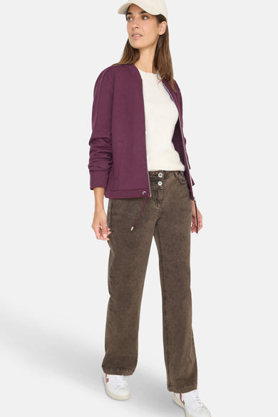 Gekleurde bruine jeans van CECIL, relaxte rechte pasvorm, gedragen met een bordeauxrode jas en een gebroken witte top.