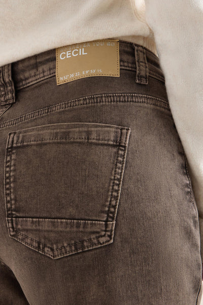 Jean coloré brun de CECIL, avec poche arrière carrée et étiquette marron à la taille, porté avec un pull blanc.
