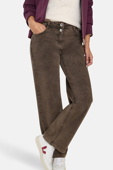 Gekleurde bruine jeans van CECIL, relaxed fit, gedragen met een crèmekleurige trui en een bordeauxrode jas.