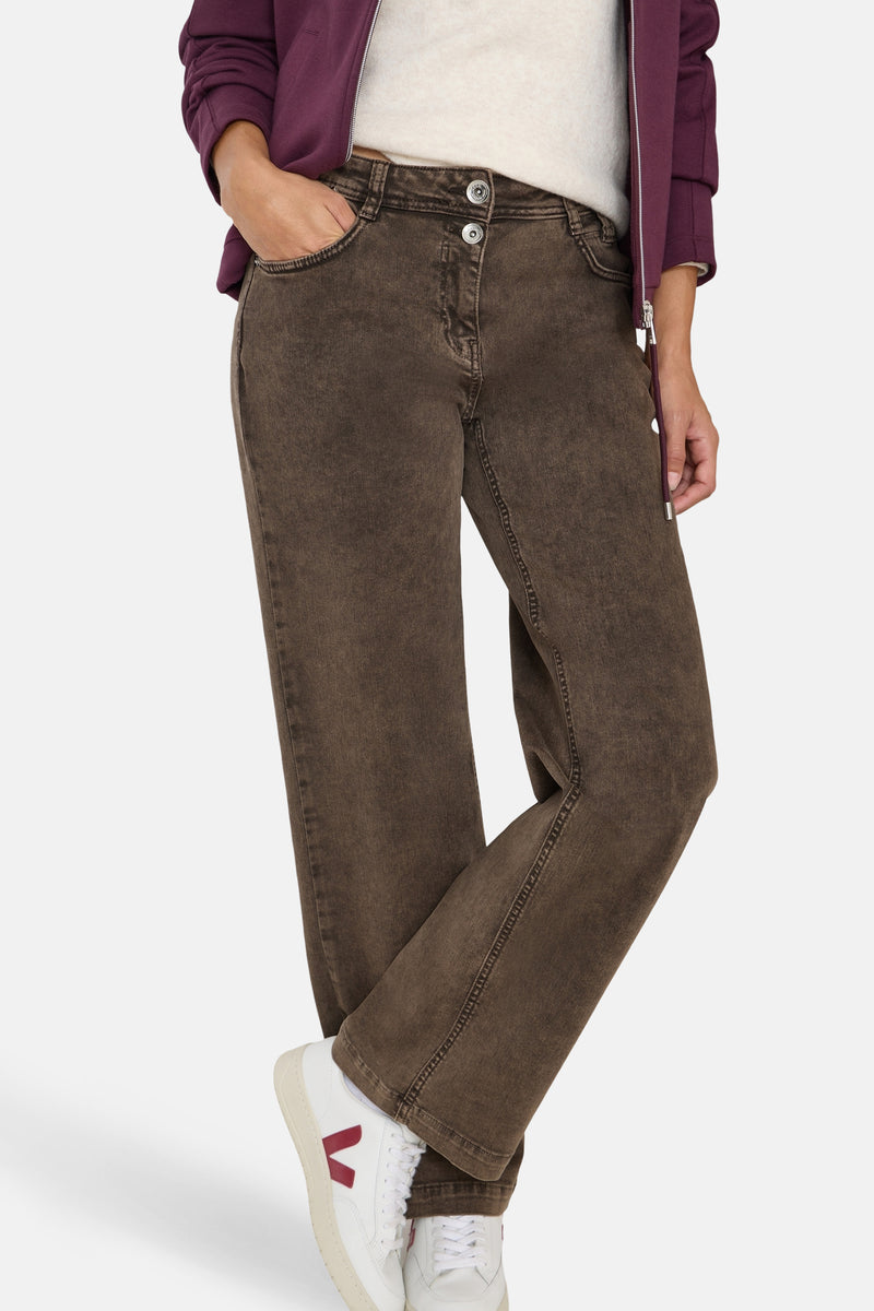 Gekleurde bruine jeans van CECIL, relaxed fit, gedragen met een crèmekleurige trui en een bordeauxrode jas.