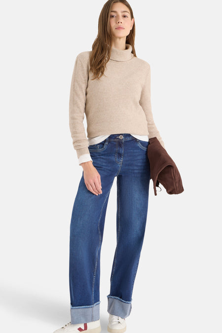Jean en denim bleu moyen par CECIL, porté avec un pull beige à col roulé et des baskets blanches.
