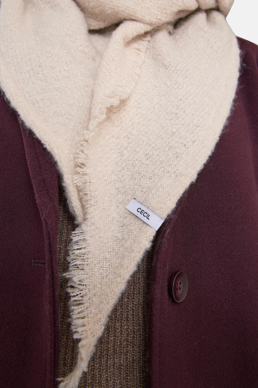 Beige sjaal van CECIL, met gerafelde randen, gedragen met een bordeauxrode jas en een bruine gebreide trui.