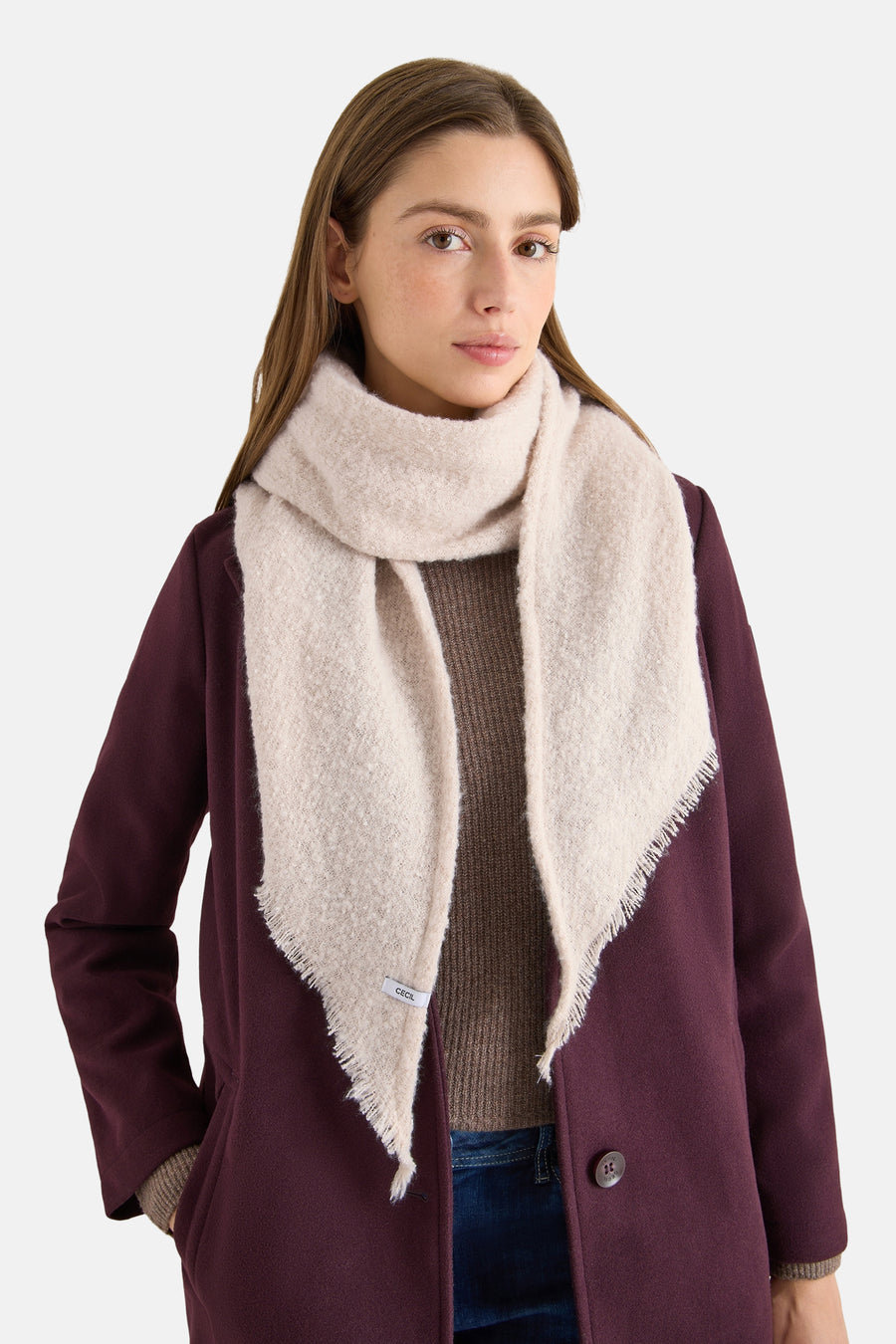 Beige sjaal van CECIL, met franjedetails en gedragen met een bordeauxrode jas en een bruine trui.