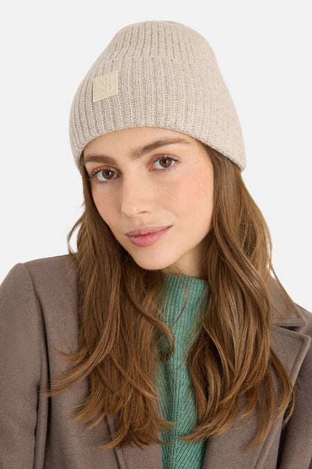 Bonnet beige en tricot de CECIL, porté avec un manteau marron et un pull vert.