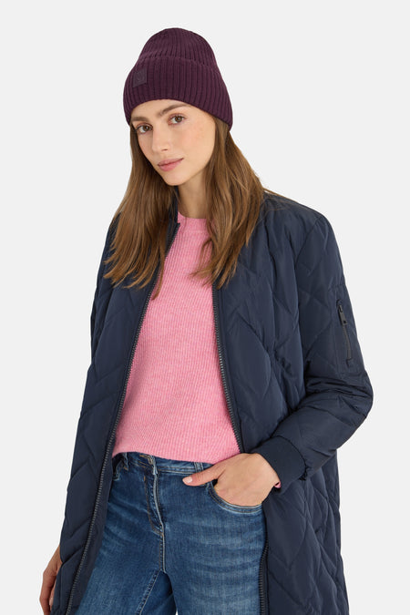 Bonnet mauve de CECIL, en maille côtelée, porté avec une veste bleu marine et un pull rose.