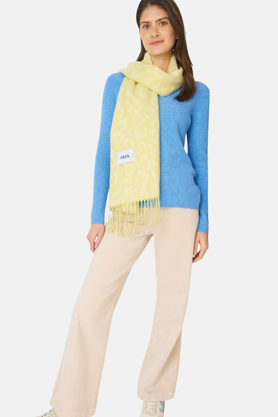 Écharpe jaune à motif léopard de CECIL, avec des franges décoratives, portée avec un pull bleu et un pantalon beige.
