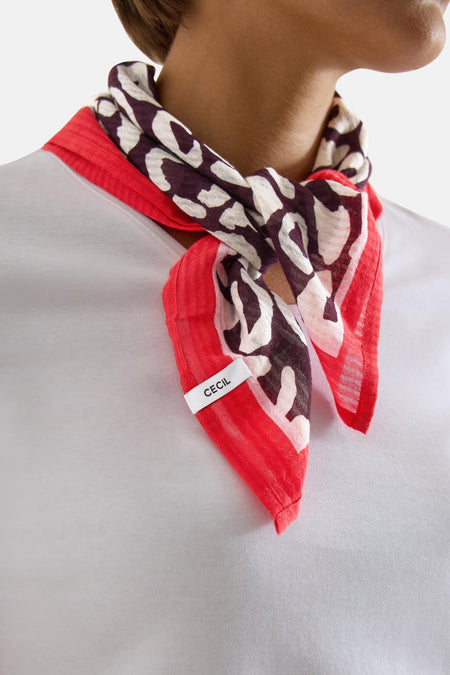 Foulard multicolore de CECIL à motifs animaliers blancs et marron avec bordure rouge, noué sur un t-shirt blanc.