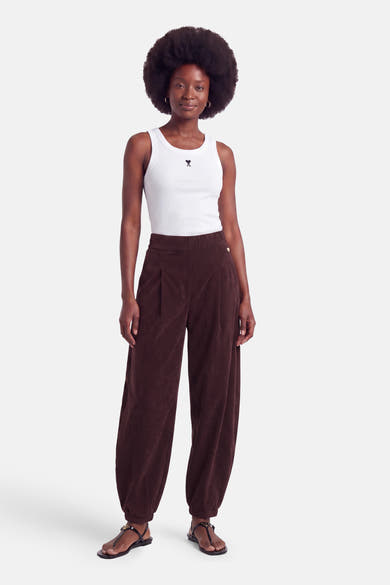 Pantalon violet en velours à taille élastique par AMELIE ET AMELIE, coupe ample avec ourlet côtelé, porté avec un haut blanc et sandales noires.