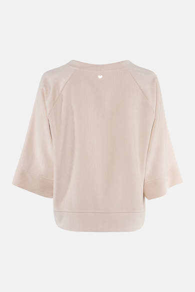 Ecru long-sleeve blouse with textured fabric and heart embellishment at back neckline, shown from rear view