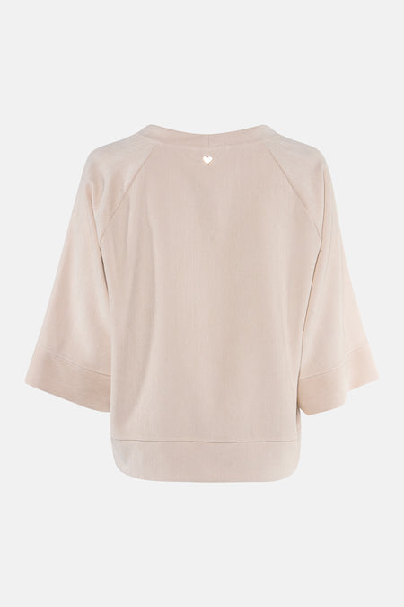 Ecru long-sleeve blouse with textured fabric and heart embellishment at back neckline, shown from rear view
