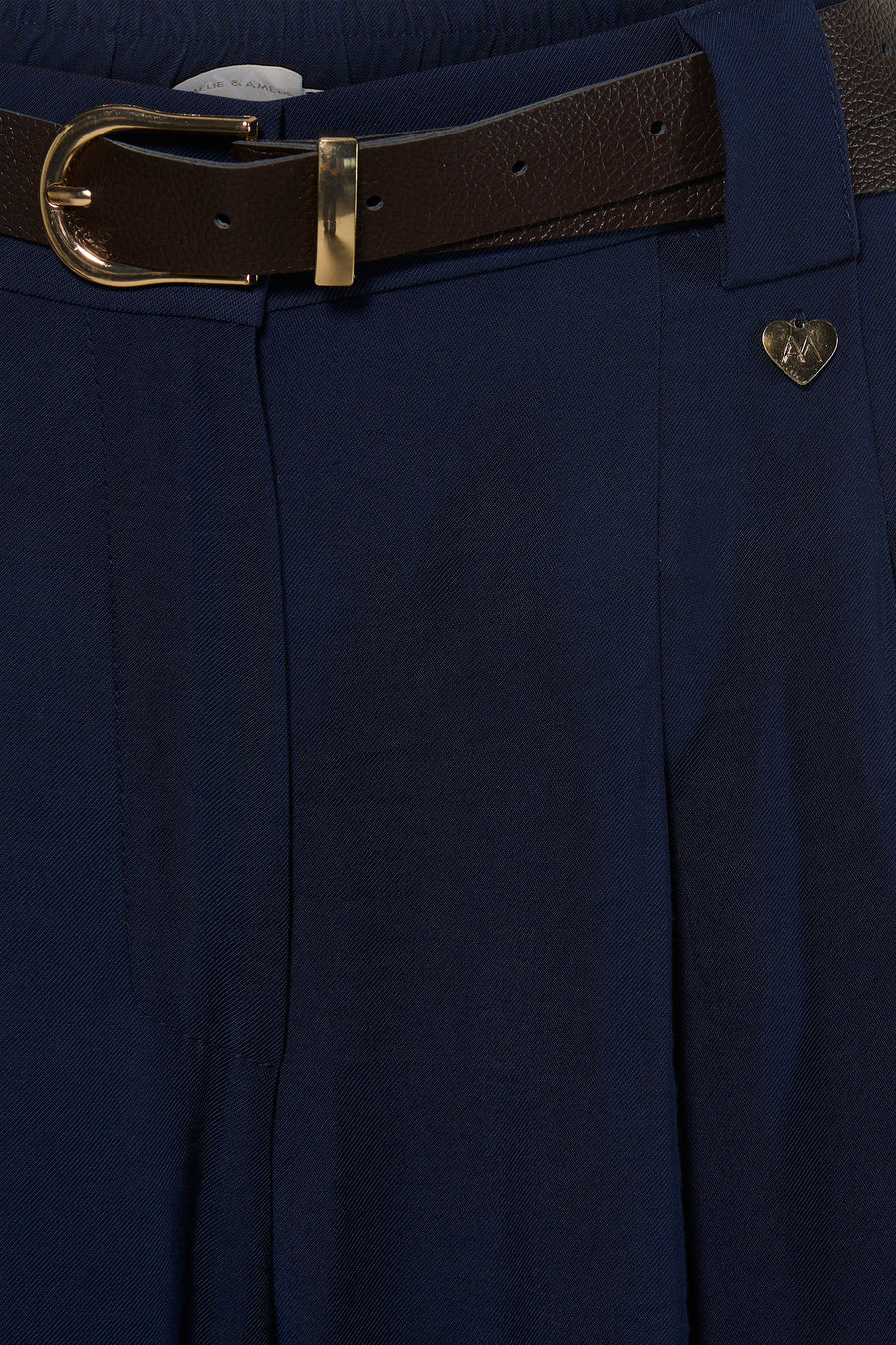 Navy blue suit trousers by Ame & Amour with textured fabric, brown leather belt, gold buckle, and heart-shaped pin detail, front close-up view