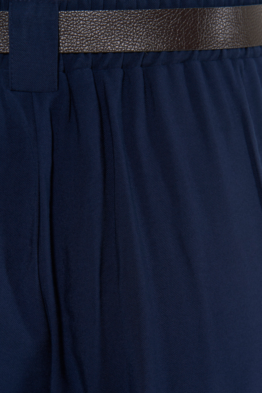 Navy blue suit trousers with front pleats and textured brown belt, close-up view