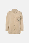 Chemise beige à manches longues de ADORE, avec poche poitrine ornée du mot « Paradise ».