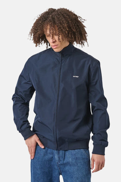 Veste de pluie bleu de ANTWRP, portée avec un jean bleu et des cheveux bouclés.