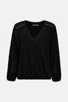 Blouse noire à manches longues de Zabaione, avec des détails plissés et des accents dorés aux épaules.
