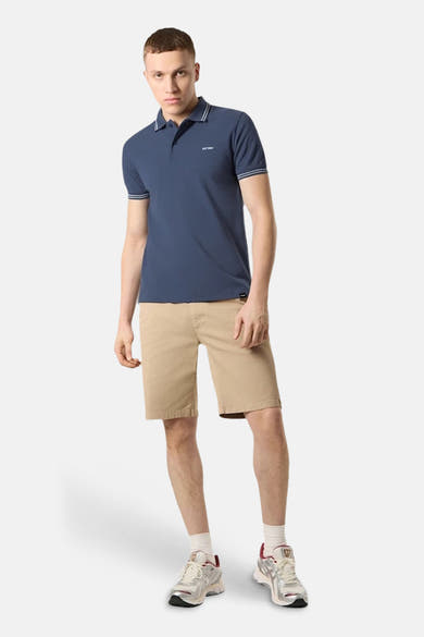Polo bleu à manches courtes de ANTWRP, avec bordures blanches au col et aux manches, porté avec un short beige et des baskets.

