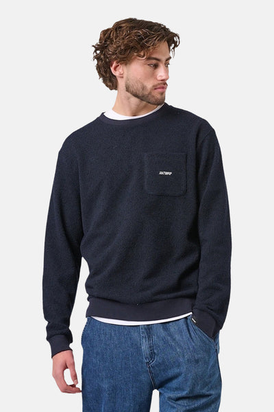 Sweat-shirt bleu de ANTWRP, avec poche poitrine et texture bouclée, porté sur un t-shirt blanc et un jean bleu.