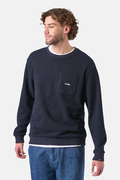 Sweat bleu van ANTWRP met poche poitrine portant le logo, porté avec un t-shirt blanc et un jean.