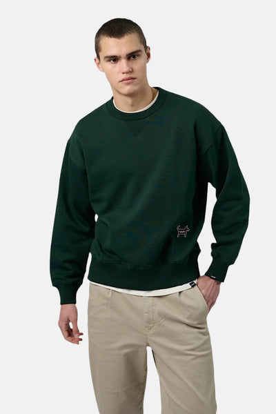 Groene trui van ANTWRP, met een klein logo op de voorkant, gedragen met een beige broek.
