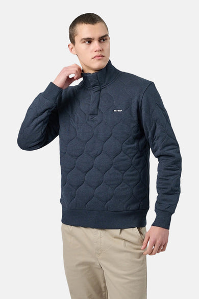 Blauwe gewatteerde sweater van ANTWRP, met opstaande kraag met drukknoopjes en gedragen beige broek.