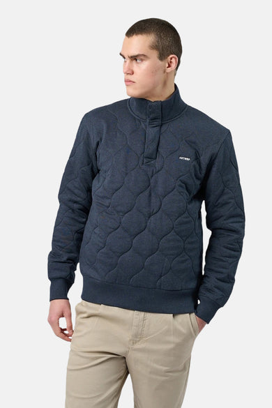 Blauwe trui met opstaande kraag van ANTWRP met ruitvormig doorgestikt patroon en beige chino broek.