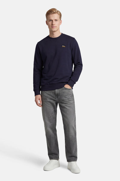 Sweat-shirt bleu de ANTWRP, avec un petit logo brodé, porté avec un jean gris et des baskets blanches.