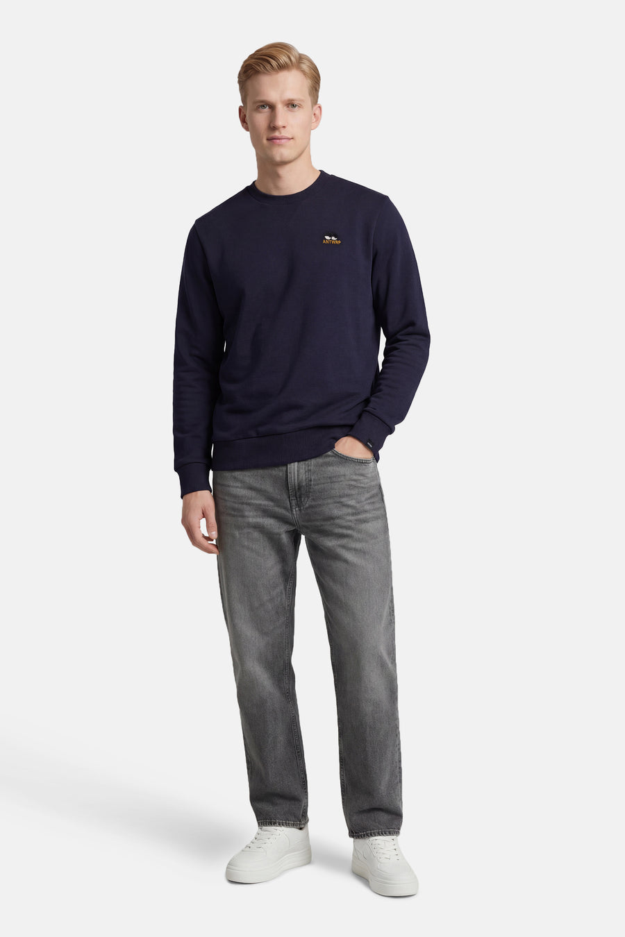 Sweat-shirt bleu de ANTWRP, avec un petit logo brodé, porté avec un jean gris et des baskets blanches.