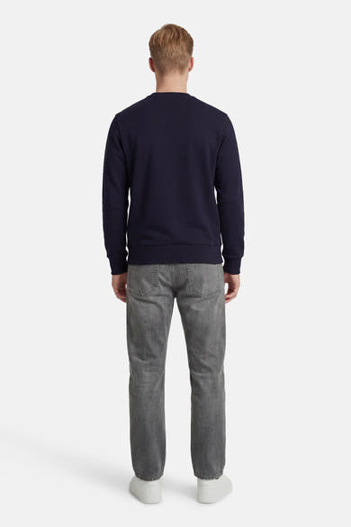 Sweat bleu de ANTWRP, porté avec un jean gris et des baskets blanches, vue de dos.
