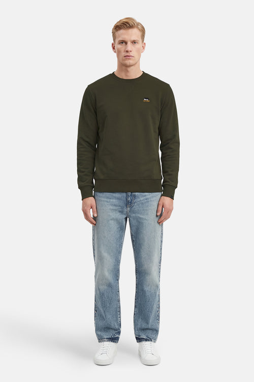 Kaki sweatshirt van ANTWRP, met geborduurd logo, gedragen met een lichtblauwe jeans en witte sneakers.